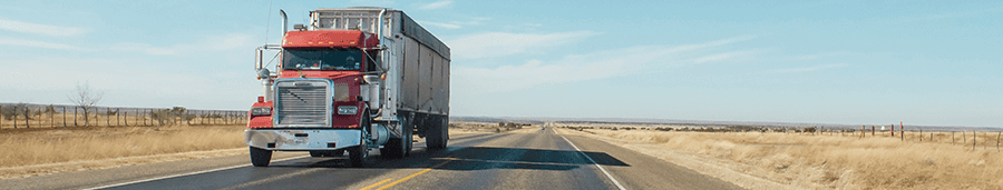 A red semi truck is driving down a highway in the desert.