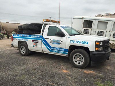 A white tow truck with tires on the back is parked in a parking lot.