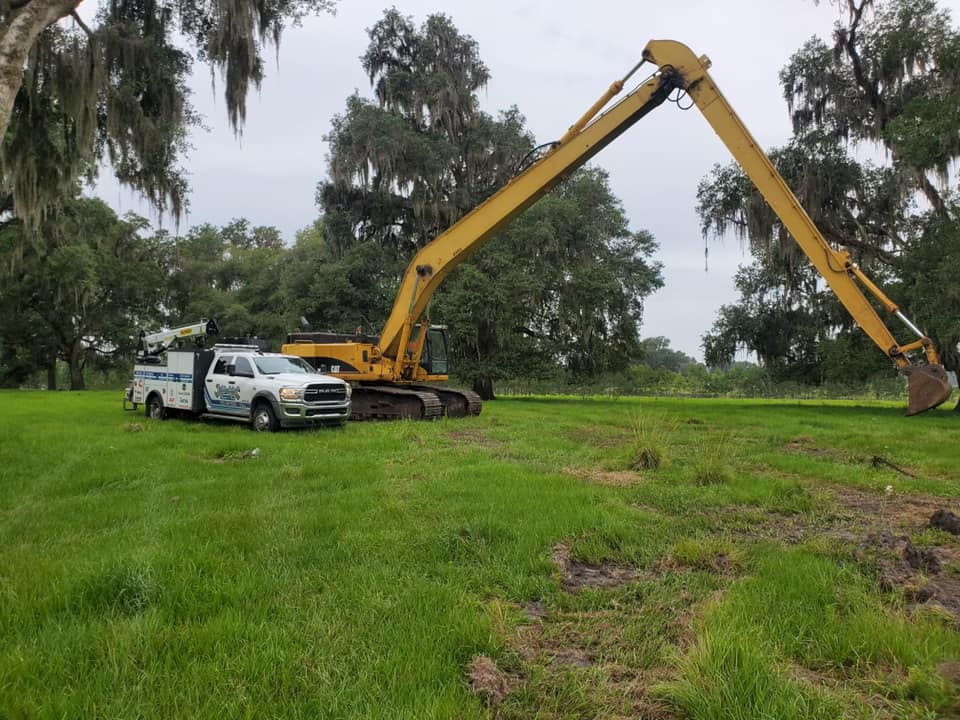A white truck is parked next to a large yellow excavator in a grassy field
