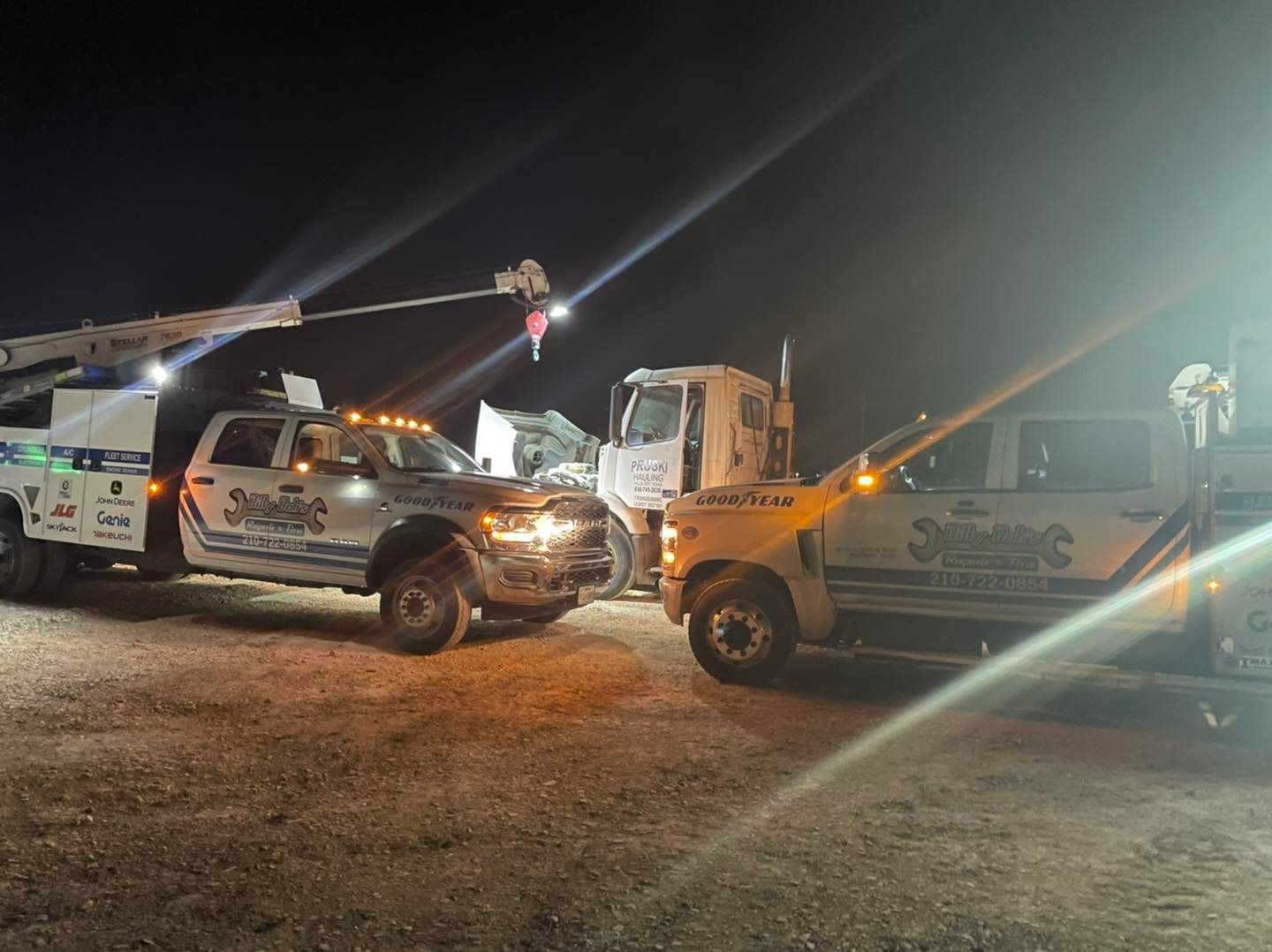 Two tow trucks are parked next to each other in a parking lot at night.