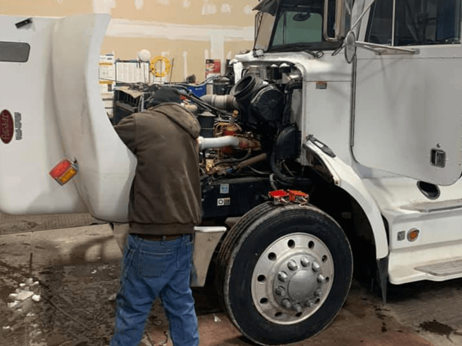 A man is working on the engine of a semi truck.
