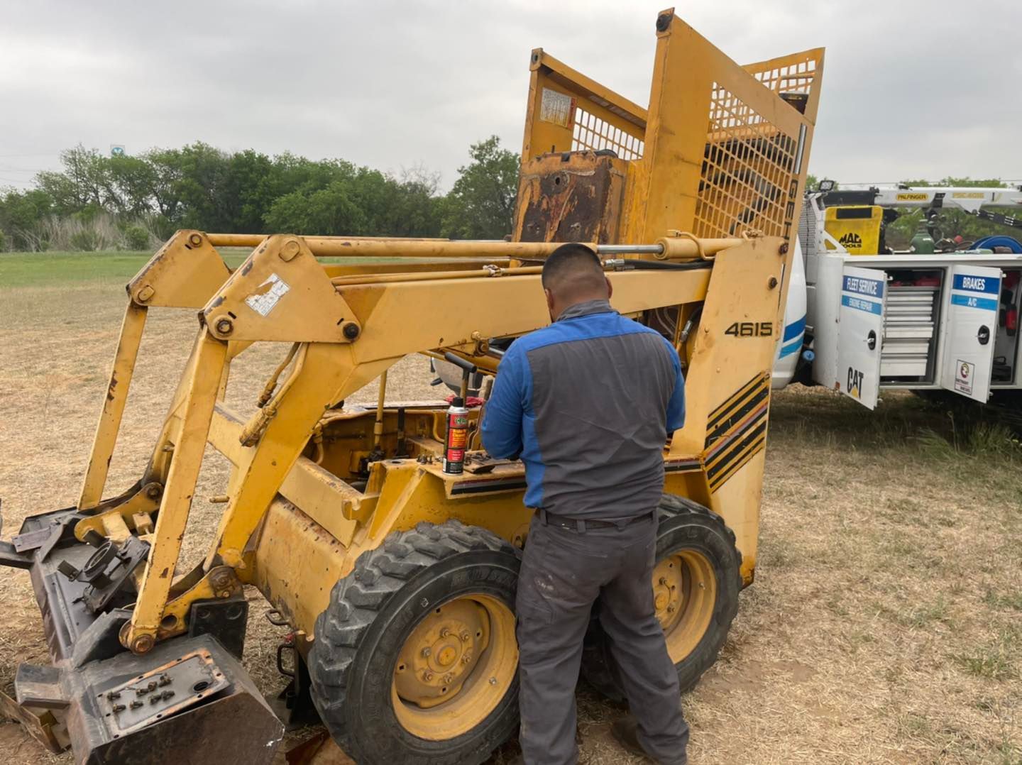 A man is working on a yellow tractor in a field.