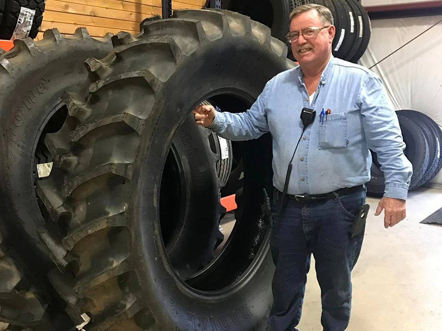 A man in a blue shirt is standing next to a large tire.