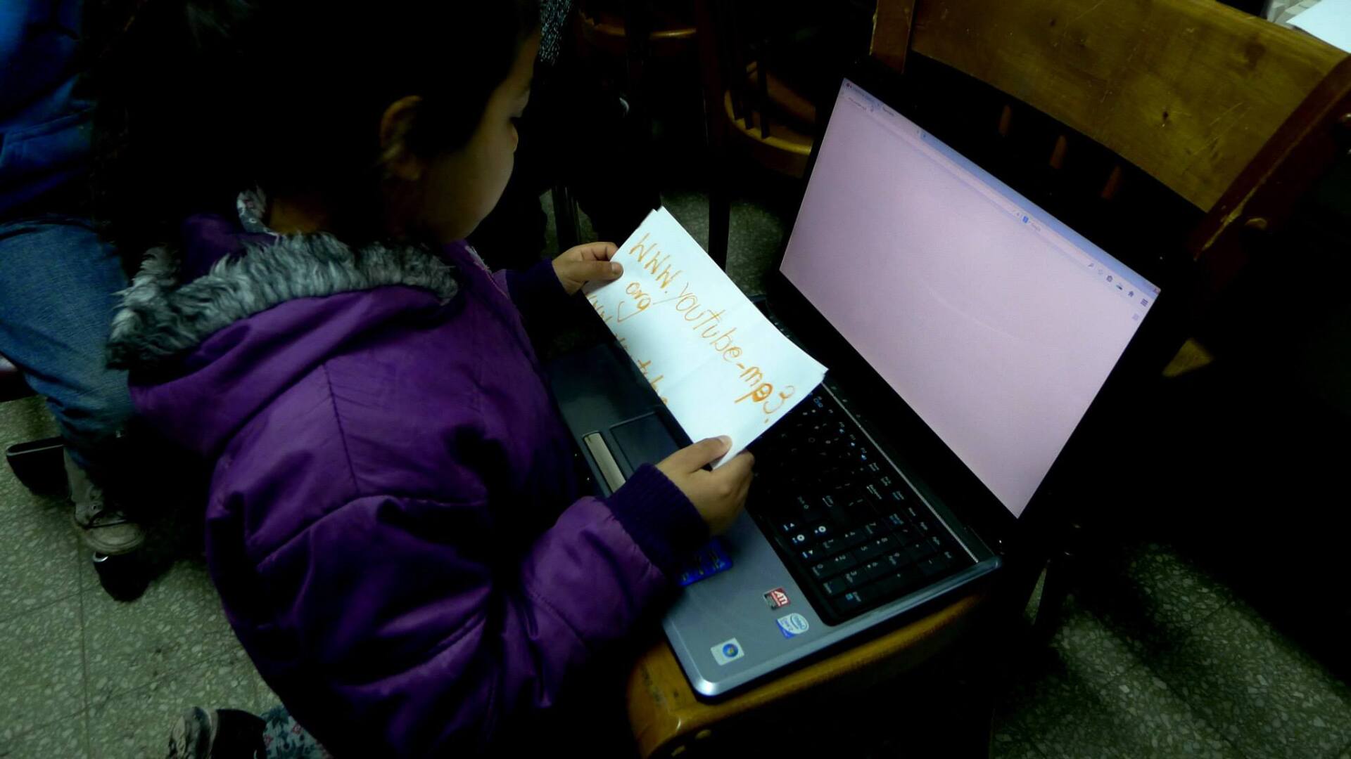 Una persona con una chaqueta violeta mira un papel frente a una computadora portátil con una pantalla blanca en blanco.