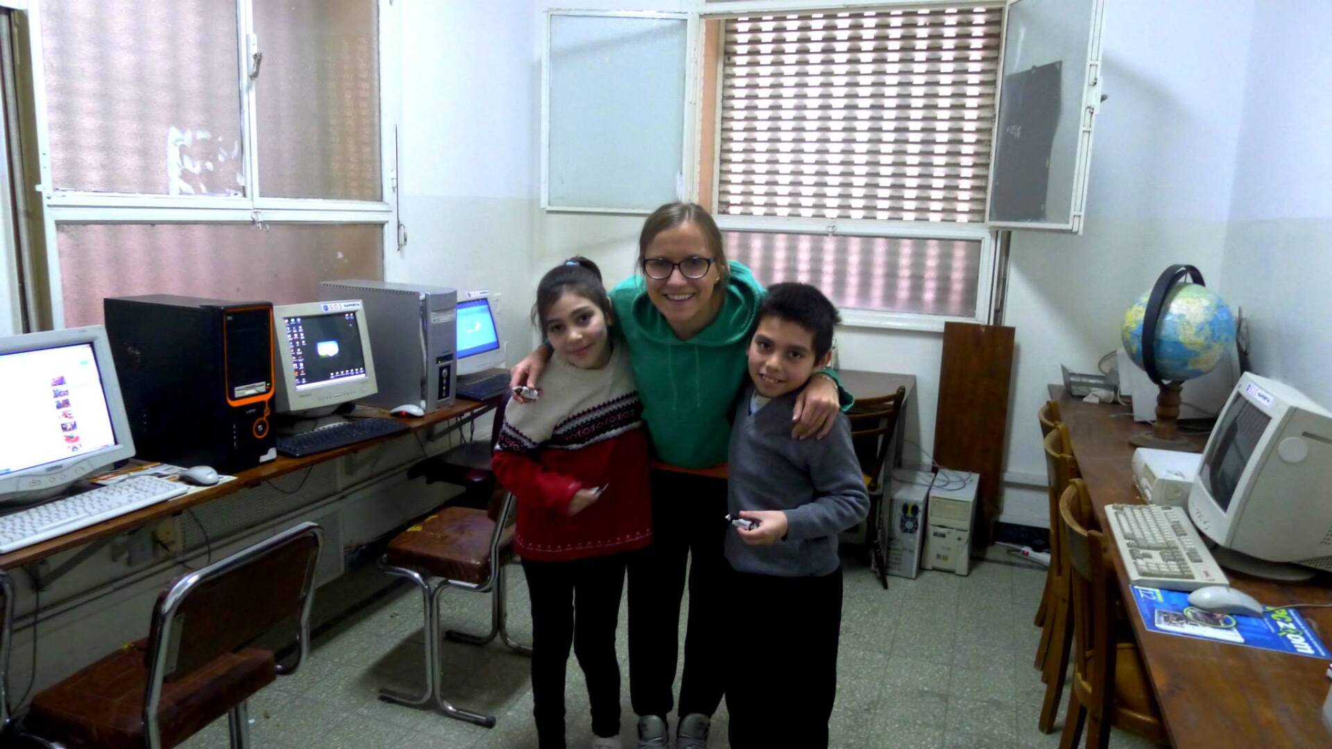 Una mujer con dos niños en un laboratorio de informática. Sonríen, de pie frente a las computadoras.