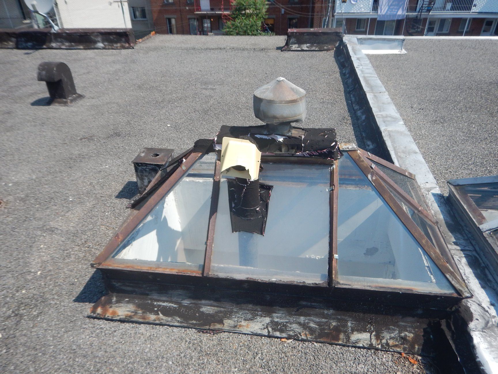 Puits de lumière sur un toit plat à l'aspect vieilli, entouré d'asphalte et doté d'un système de ventilation.