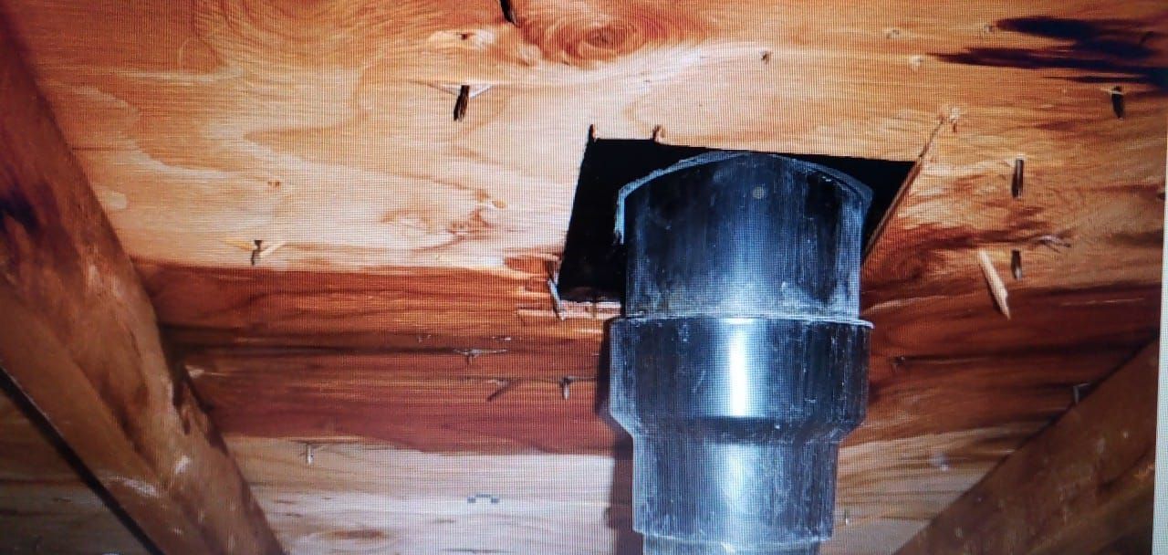 Un tuyau noir traverse un plafond en bois dans un grenier. Le bois semble être teinté.