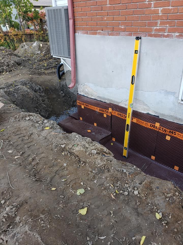 Étanchéité des fondations par membrane granuleuse brune. Niveau à bulle fixé. Terrassement visible.
