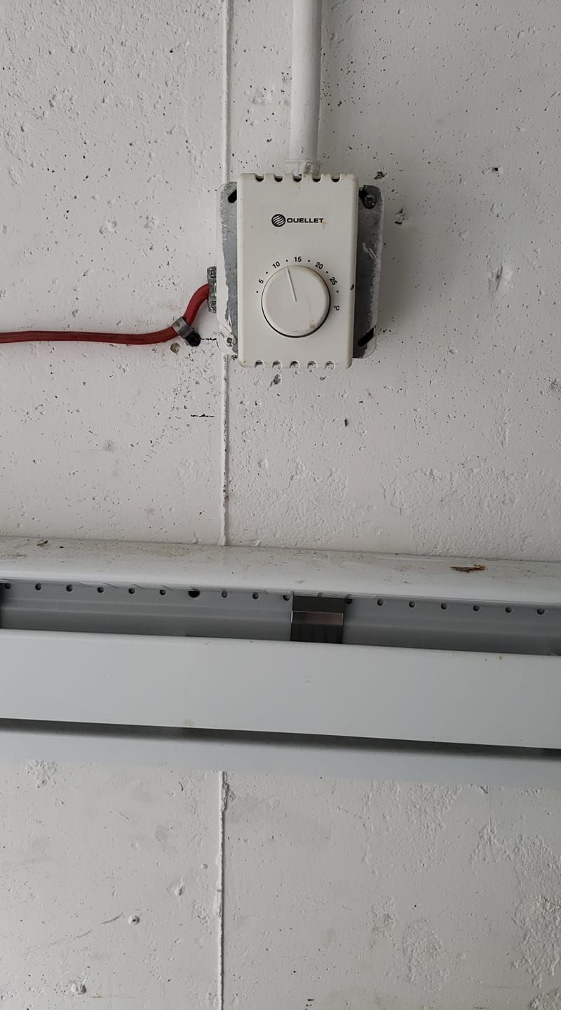 Mur blanc avec thermostat, conduit électrique et plinthe chauffante.
