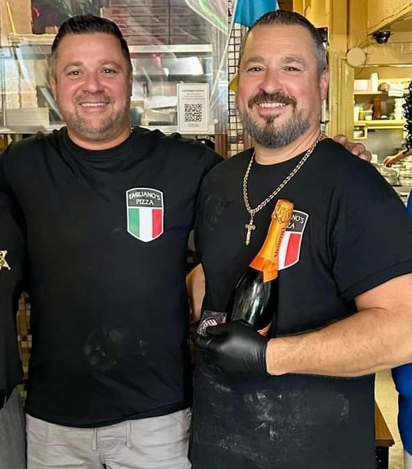 Two men posing for a picture with one holding a bottle of wine