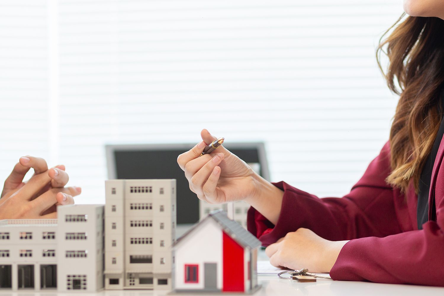 Real estate agent hands a house key to a client over miniature buildings.