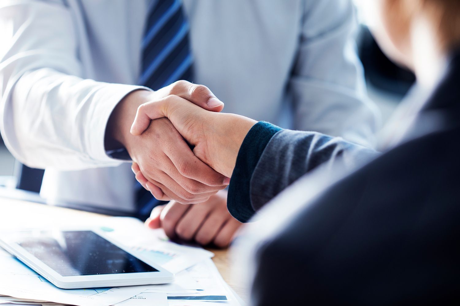 Two people shaking hands over a desk, business agreement.