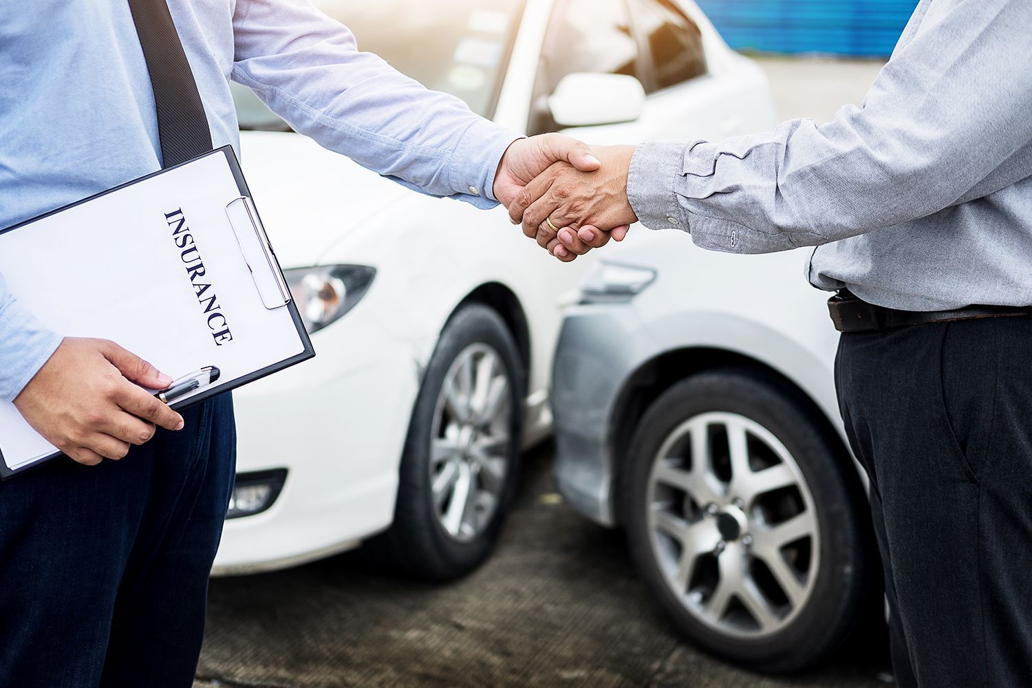 Two men shaking hands beside damaged cars; one holds an insurance form.