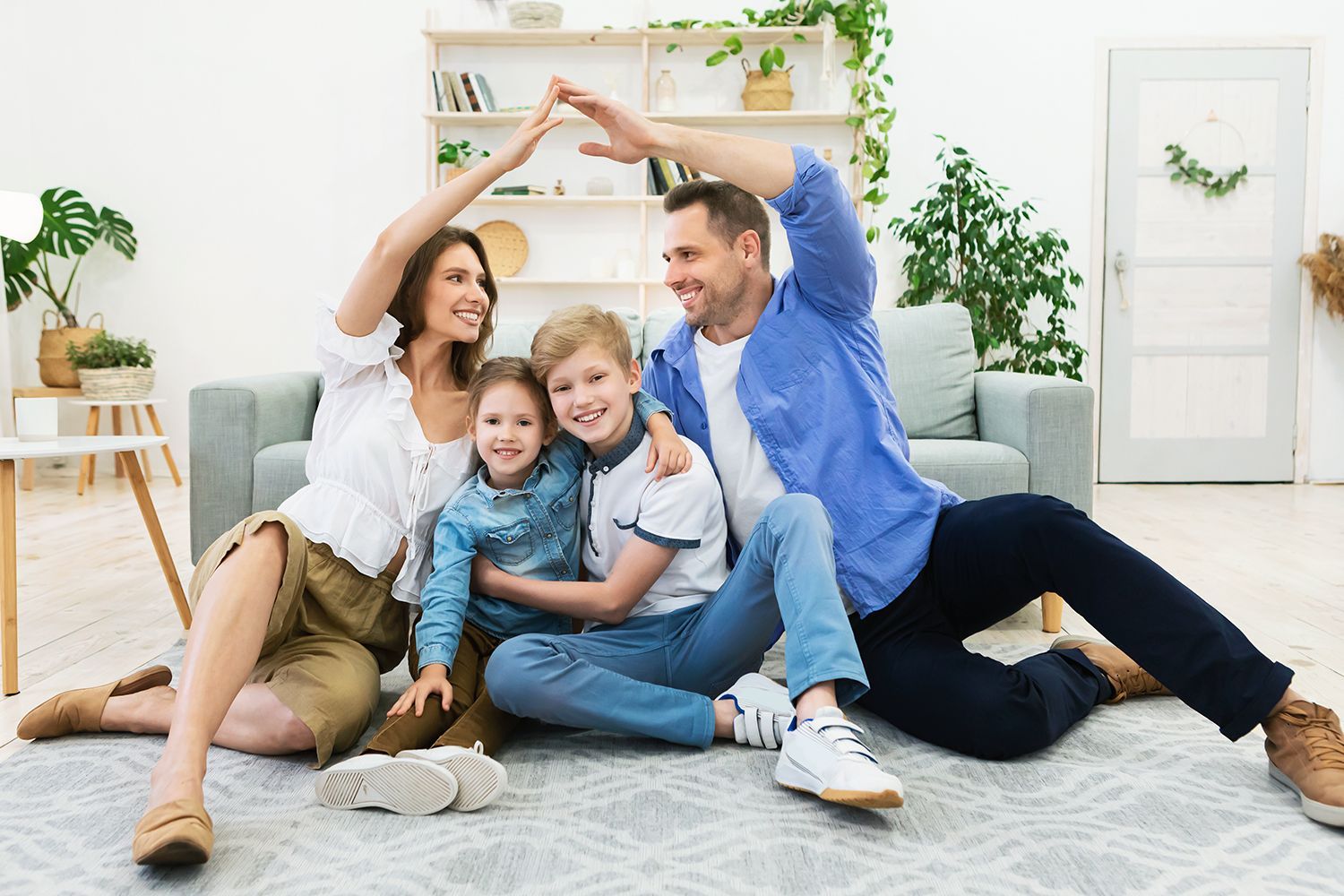 Family making a roof shape with their arms indoors, smiling, on a rug.