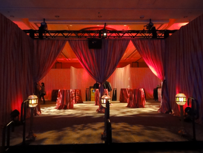 Stage with red-lit drapes, tables, and lanterns. People stand on the stage.
