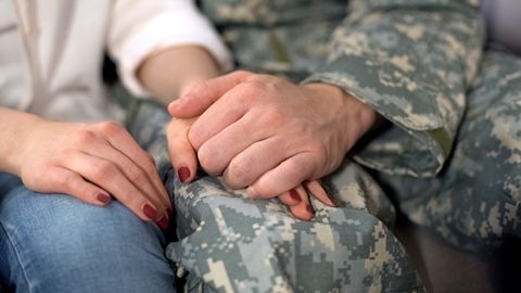 Person in military uniform and civilian holding hands, close-up.