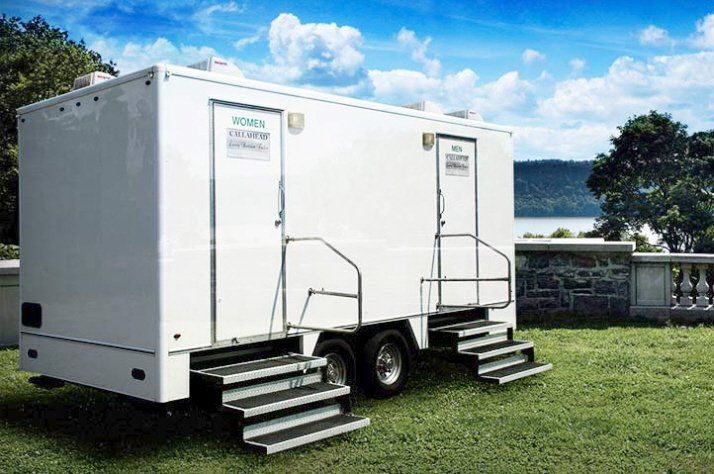 The Guide to Event Portable Toilets advises how to choose the right style & quantity of luxury portable toilet rentals, featuring a portable toilet calculator. a white trailer with two toilets on it is parked in a grassy field .