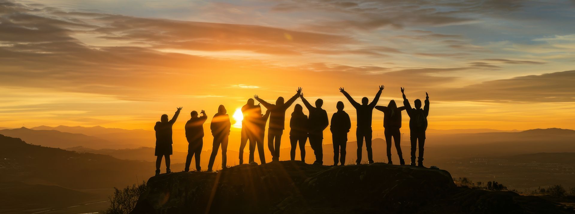 Silhouetted group of people on a hill at sunset, arms raised against an orange sky