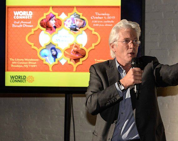 Man speaking at event with event graphic: orange background, colorful cartoon images.