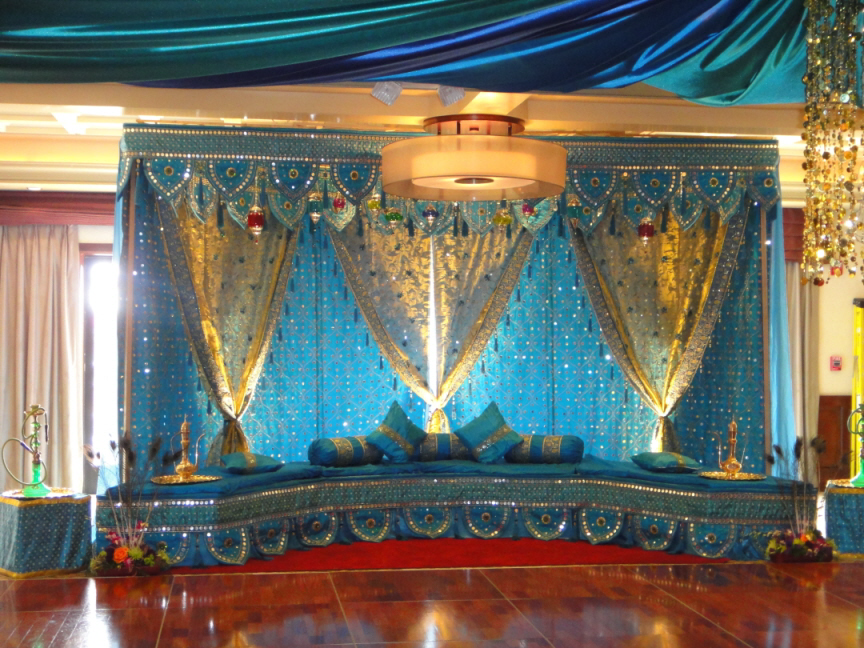 Turquoise stage with gold trim, drapes, and cushions; red carpet; wooden floor.