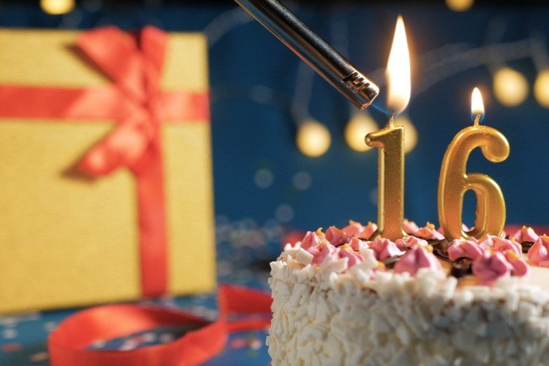 Image showing wrapped gift and birthday cake with numeric candles being lit showing  16