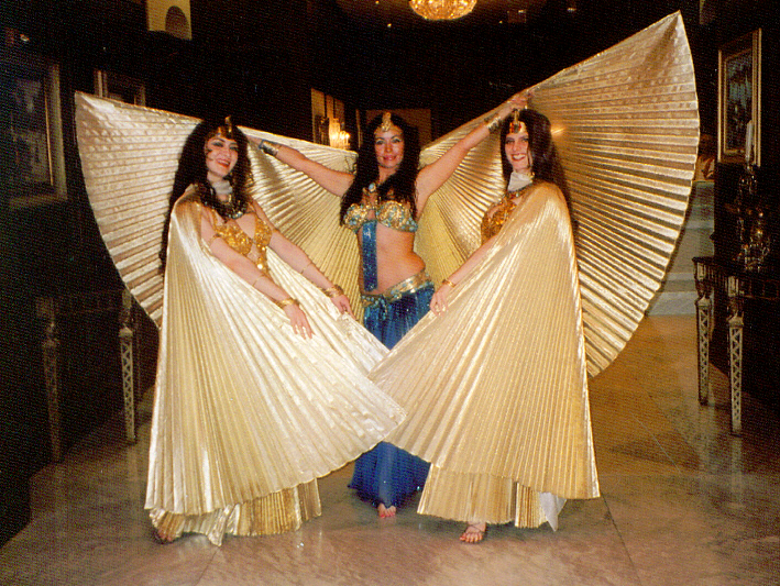 Three dancers in gold costumes and wings, posing with arms outstretched, indoors.