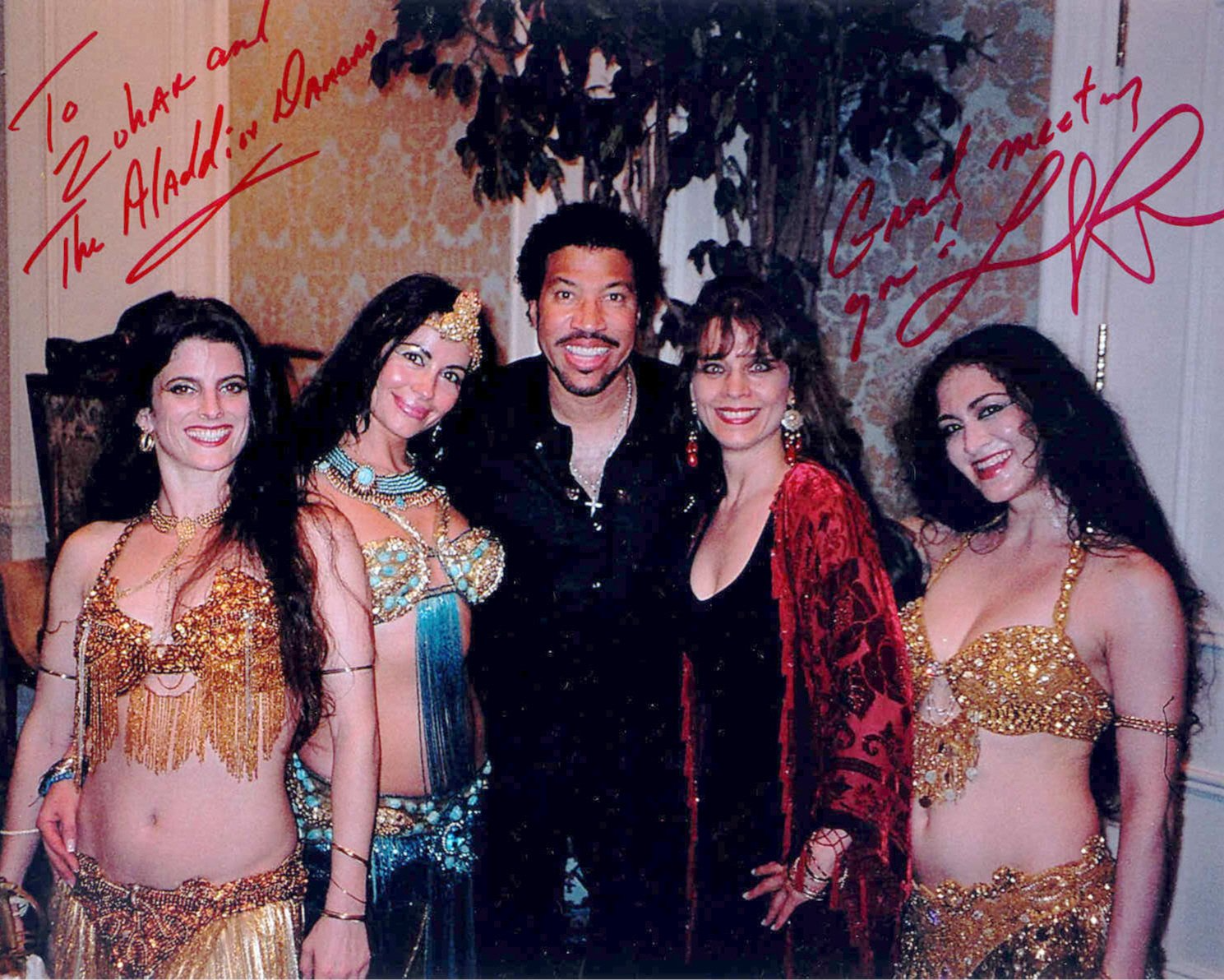 Lionel Richie with belly dancers, posing for photo. Signed autographs, formal setting.