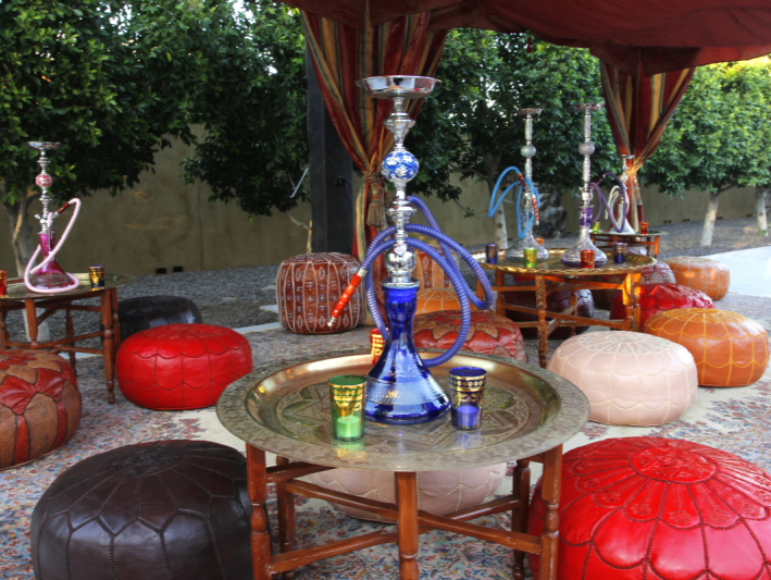 Hookah lounge: ornate hookahs on tables, surrounded by colorful poufs and canopy.