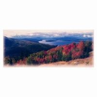Panoramic view of a mountain range with autumn trees in shades of red and lake in the distance.