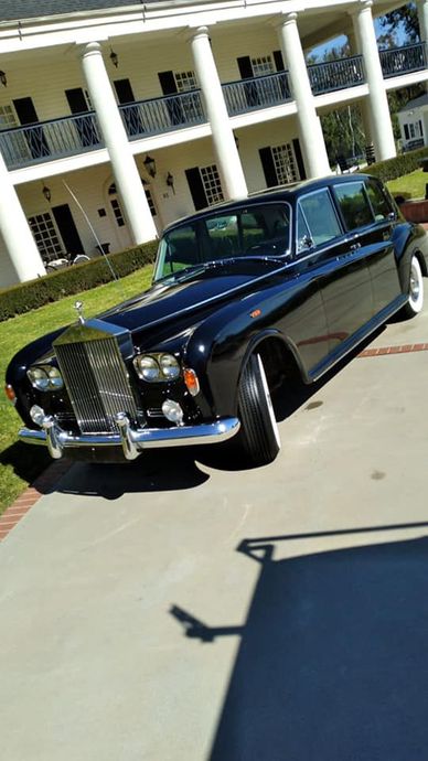 Black classic Mercedes-Benz sedan parked in front of a white-columned building on a sunny day