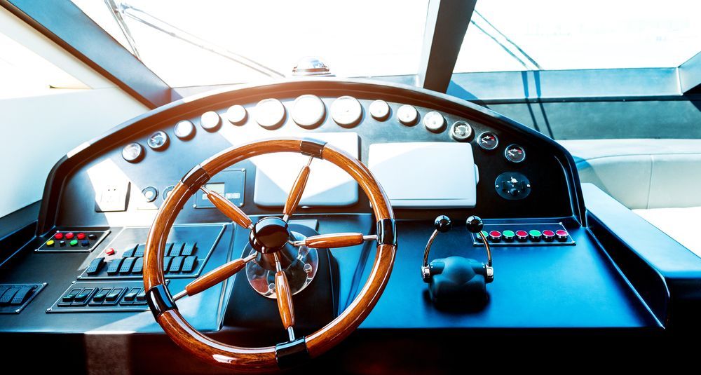 Steering wheel and helm controls on a boat dashboard with blue panels and nautical gauges