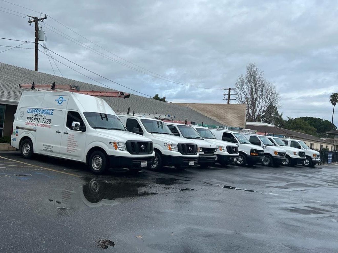 Fleet of white service vans parked in a wet lot under an overcast sky