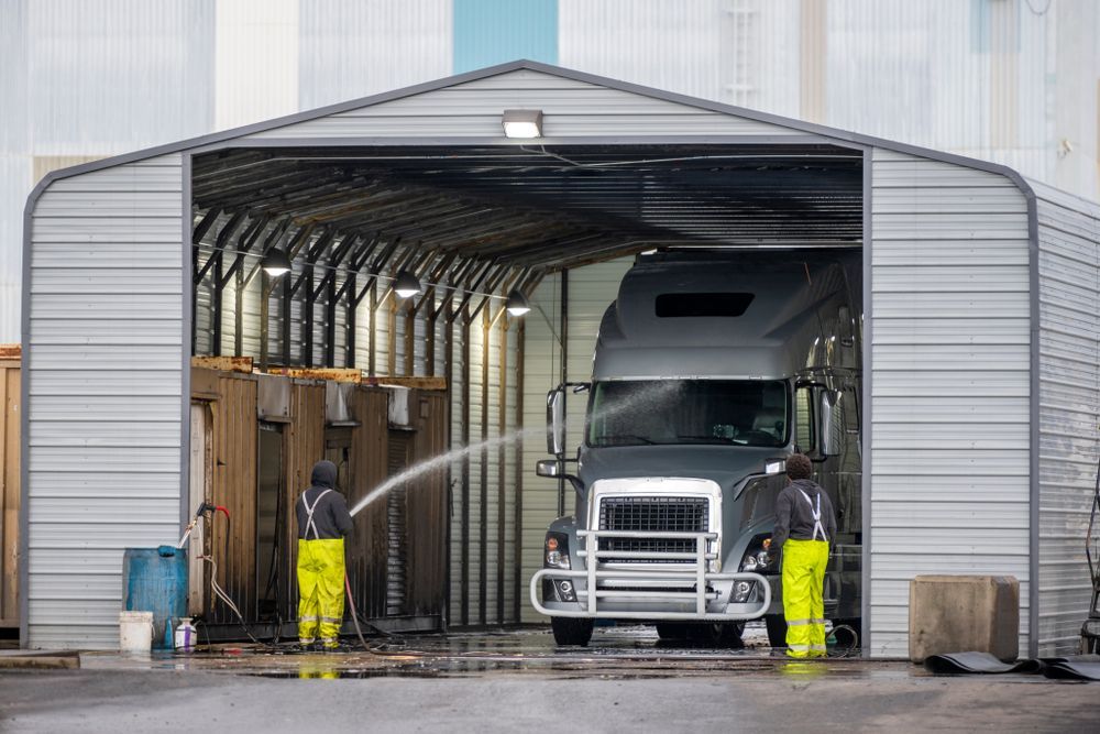 Truck being washed in a large industrial wash bay by two workers in yellow pants