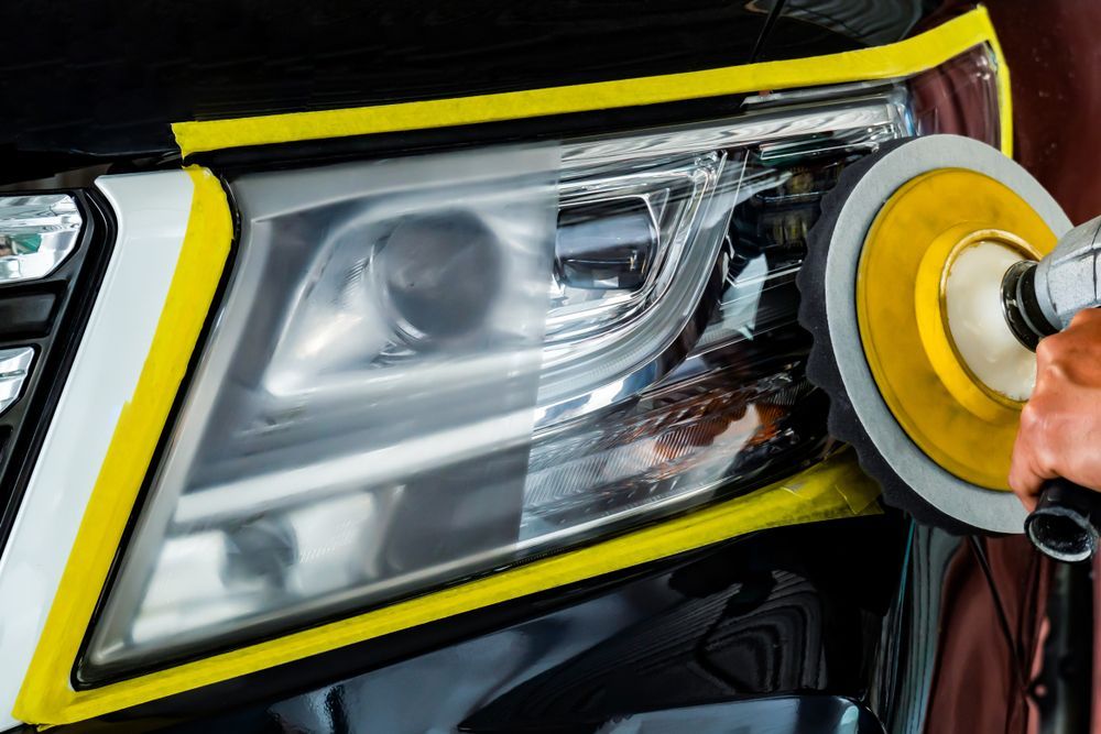 Person polishing a car headlight with a yellow buffer and cloth