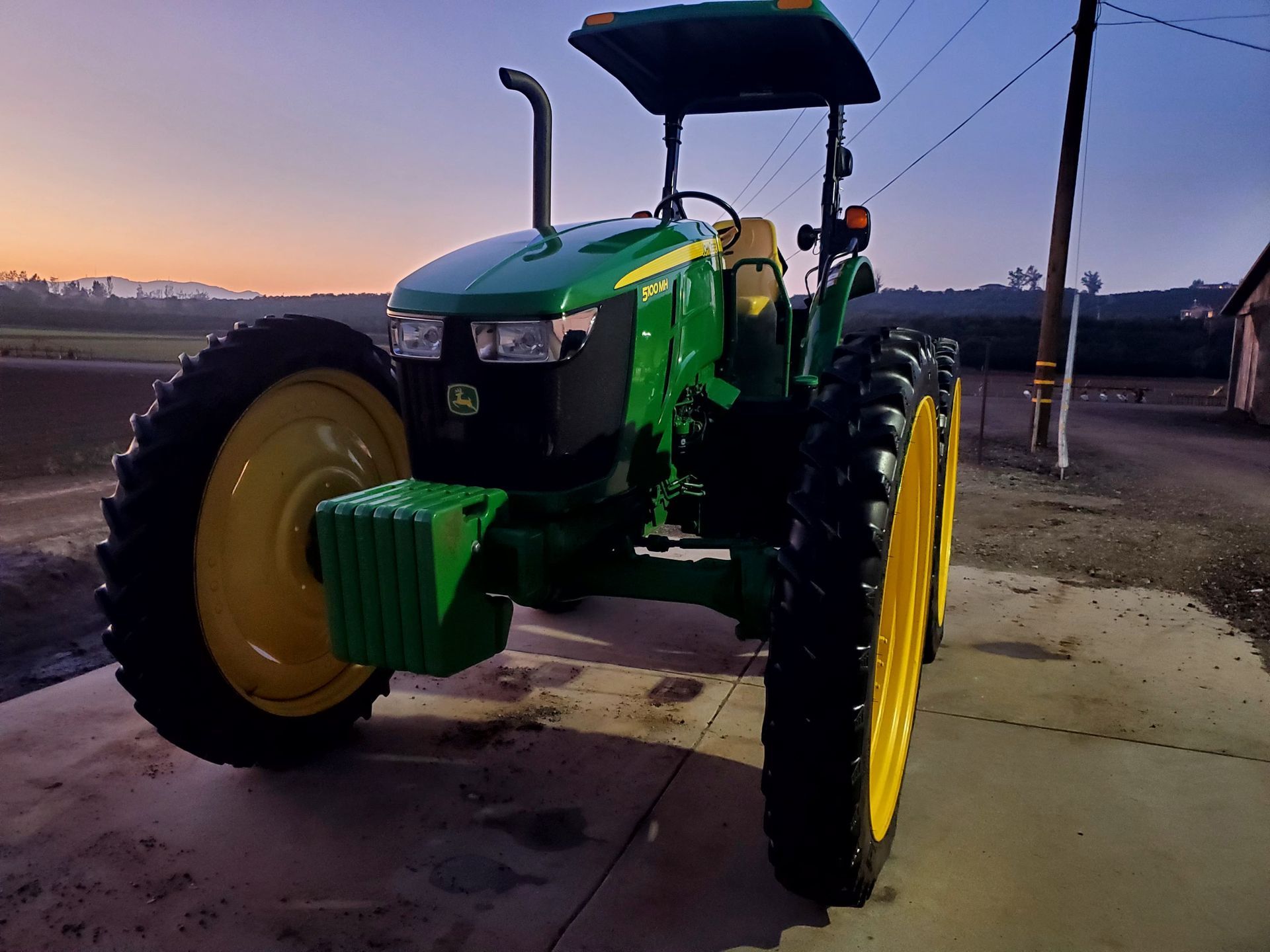 Green tractor with yellow wheels parked outdoors at dusk