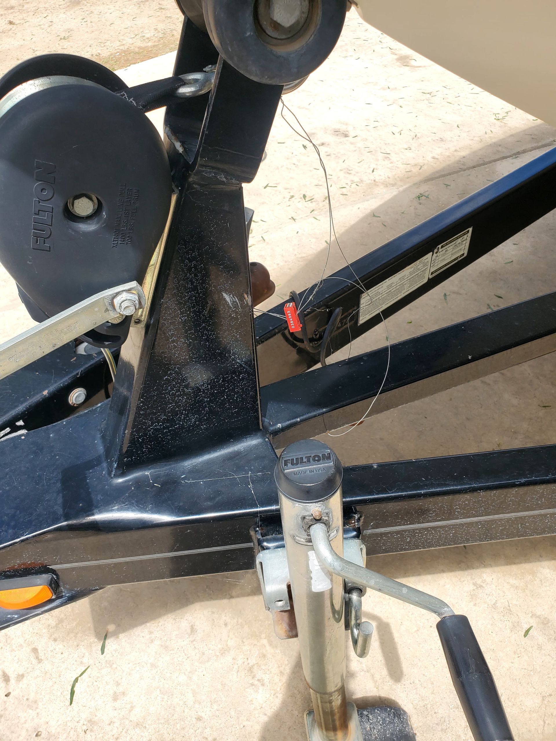 Close-up of a black metal trailer hitch with a coupler and safety chains on pavement