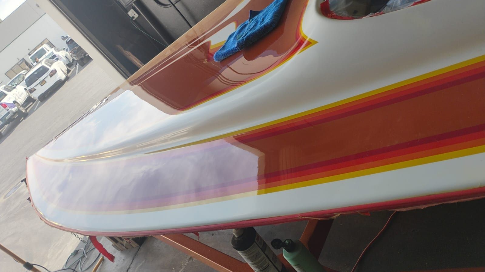 Long white-and-red boat hull on a trailer in a parking lot, viewed close-up from the side.