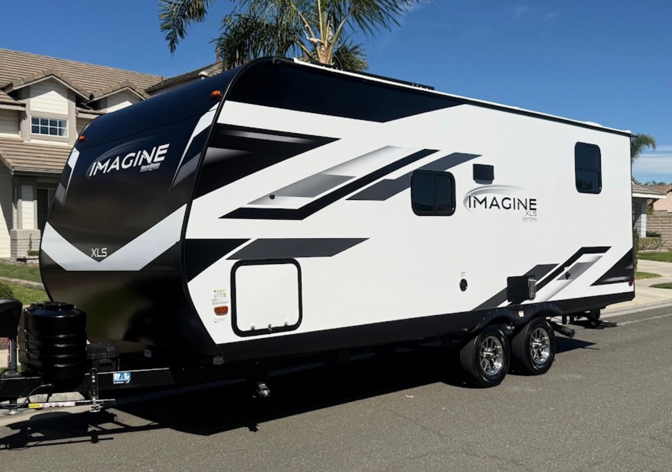 White and black Imagine ZM travel trailer parked on a street under a blue sky.