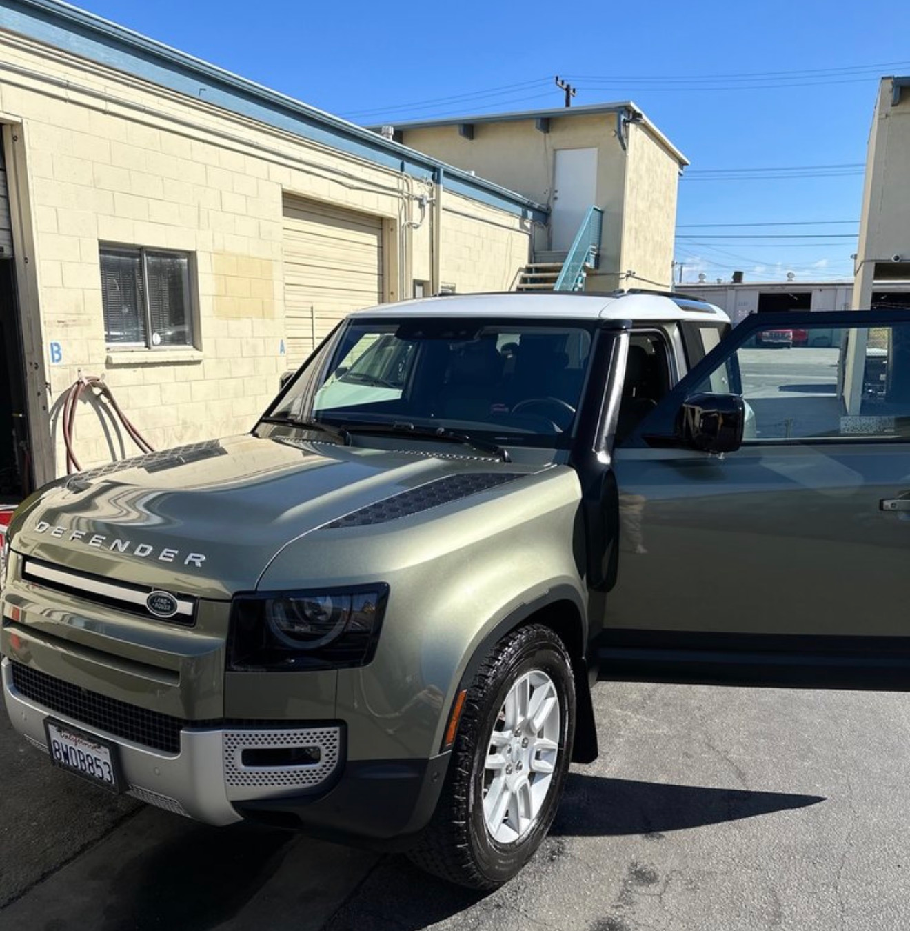 Gray Land Rover SUV parked outside a building with the driver’s door open on a sunny day