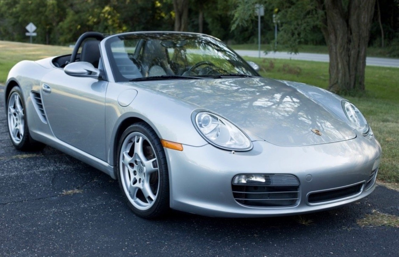 Silver Porsche convertible parked on a roadside with trees in the background