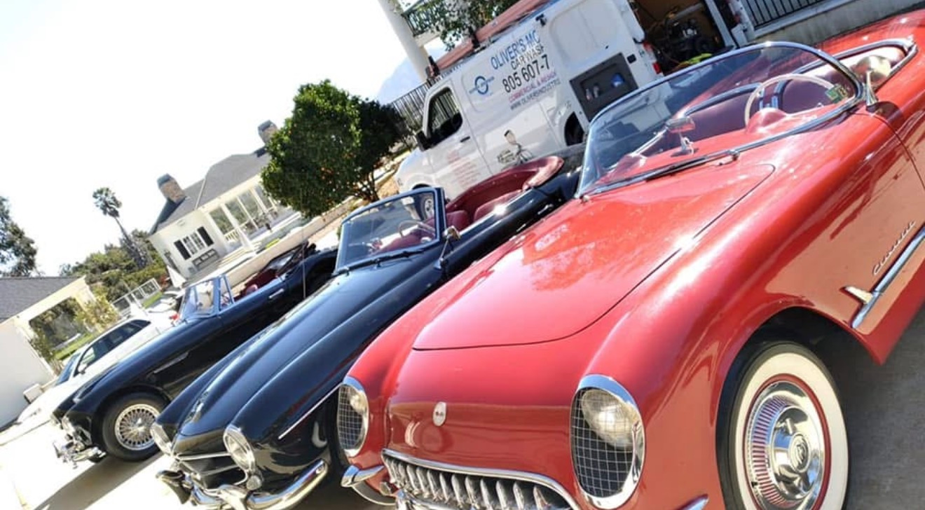 Three classic convertibles parked side by side, including a red car in the foreground.