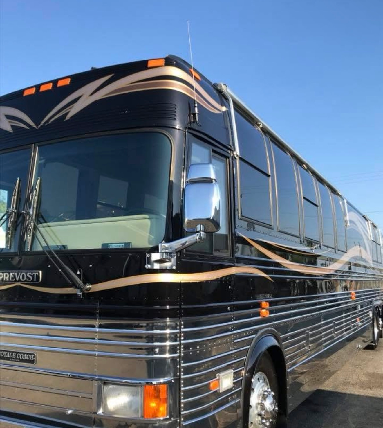 Black and gold Prevost luxury coach bus parked outdoors under a clear blue sky