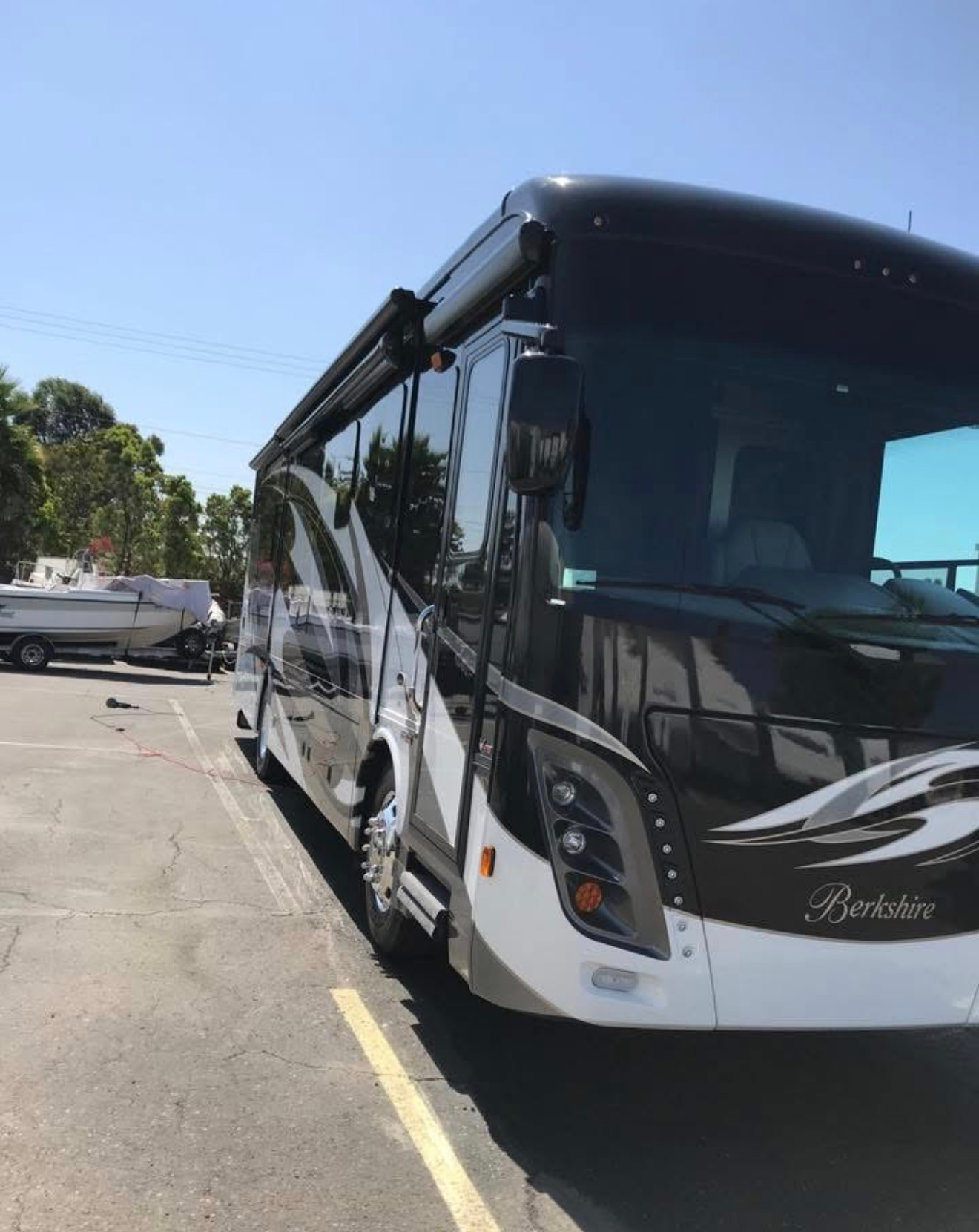 White luxury coach bus parked in a sunny lot beside a yellow line.