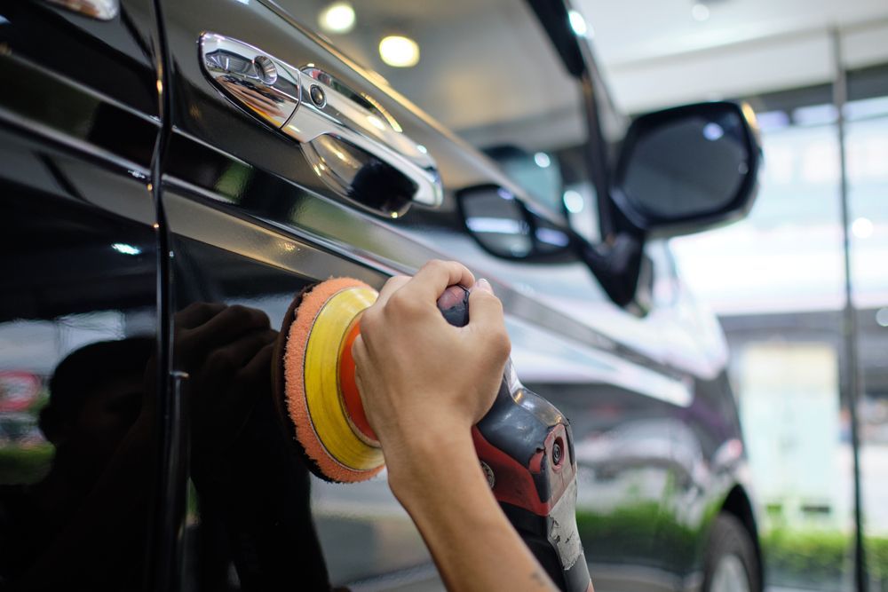 Hand polishing a black car with a red and yellow buffer pad