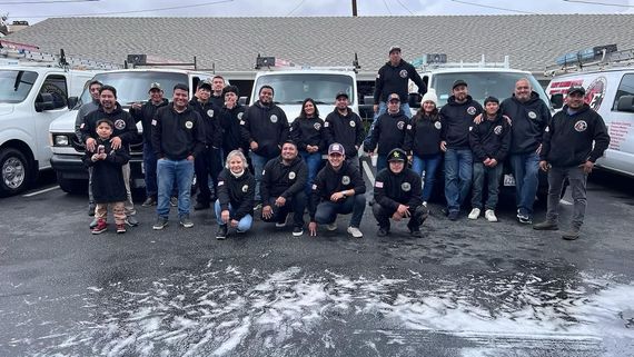 Group of people in black jackets posing outdoors in snowy weather in front of a stadium wall