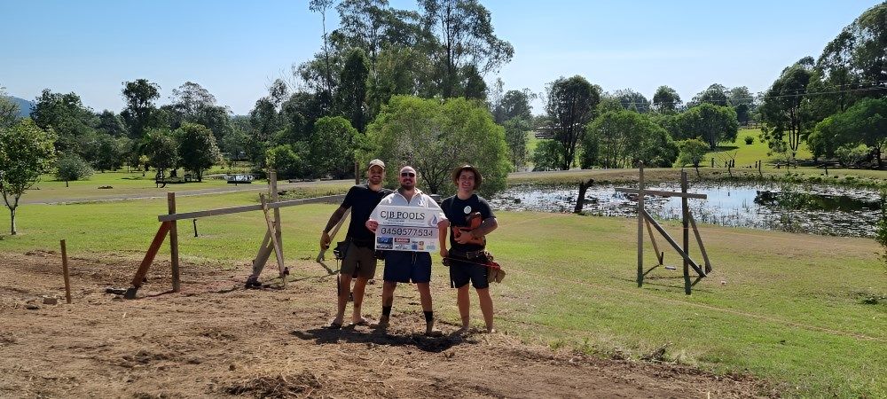 Three People Are Standing In A Field Holding A Sign — CJB Pools in Gympie, QLD