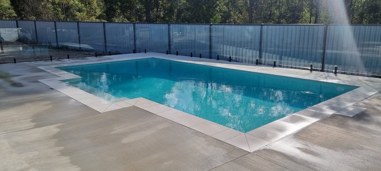 A Large Swimming Pool Surrounded By A Fence And Trees — CJB Pools in Veteran, QLD