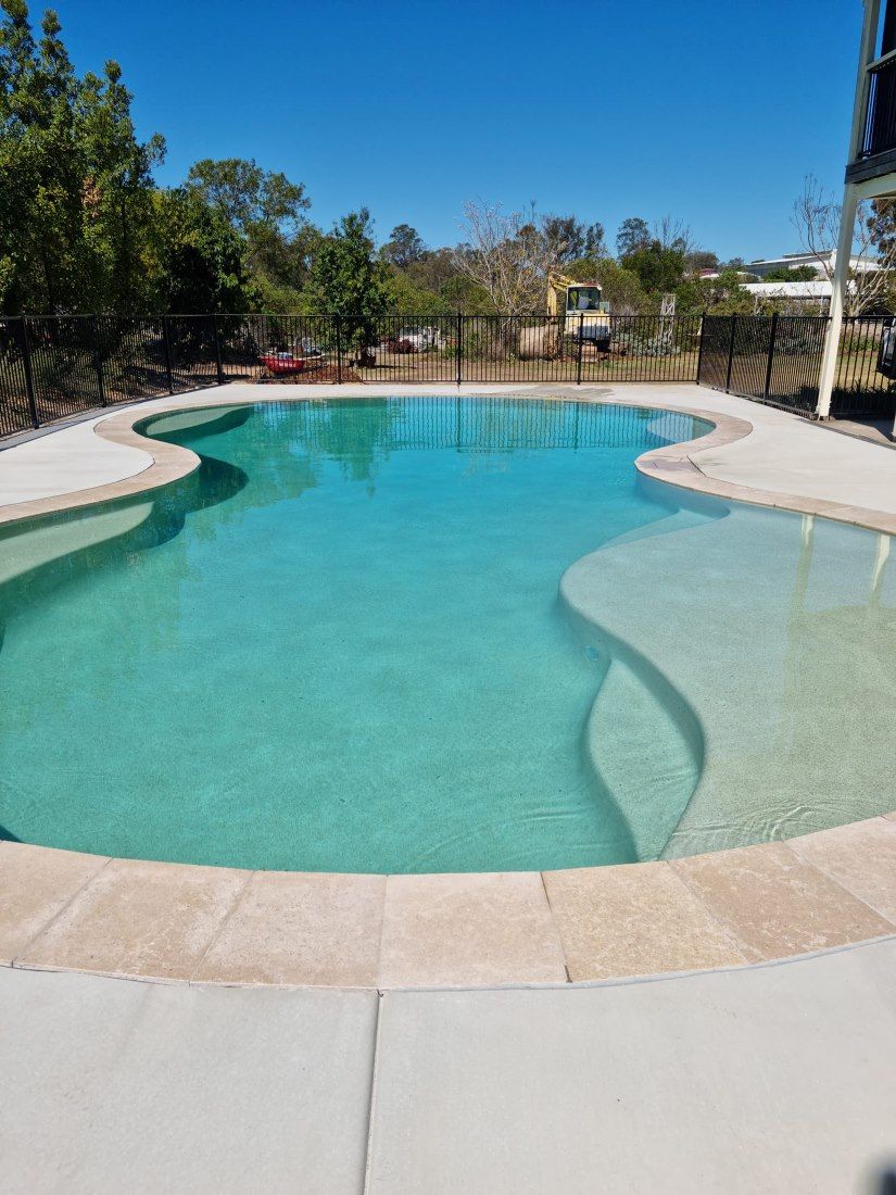 A Large Swimming Pool Surrounded By Trees On A Sunny Day — CJB Pools in Cooroy, QLD