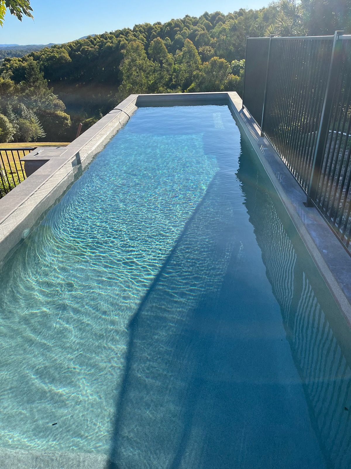 A very long swimming pool with a view of a forest — CJB Pools in Gympie, QLD