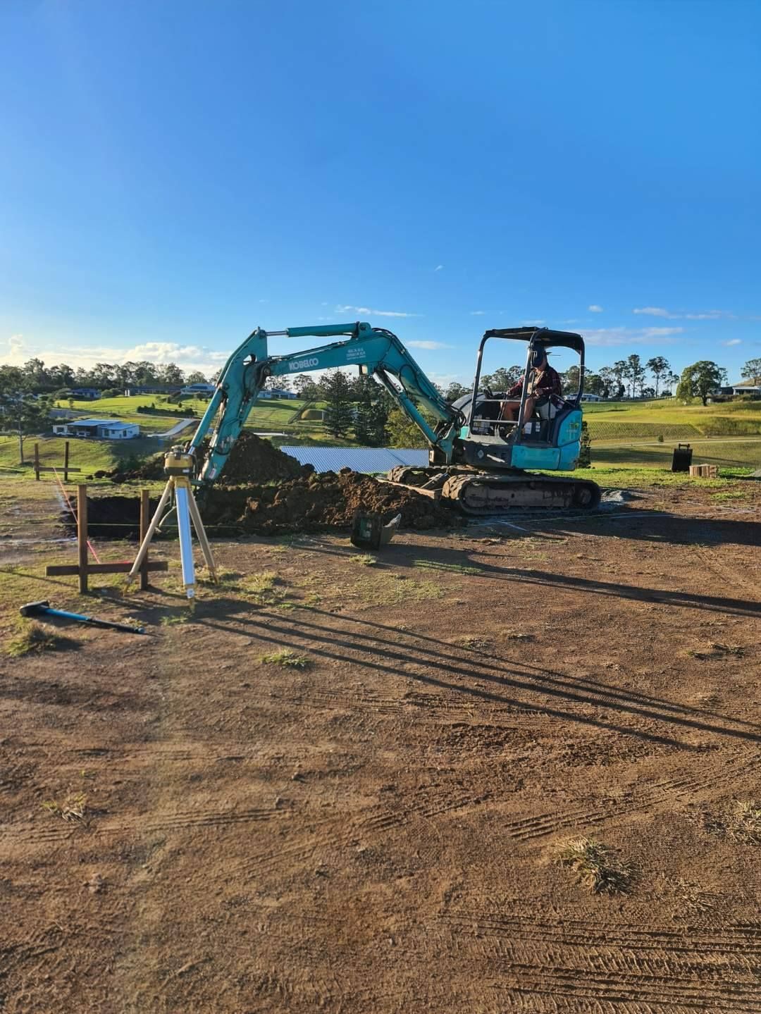 A man is driving an excavator in a dirt field — CJB Pools in Gympie, QLD